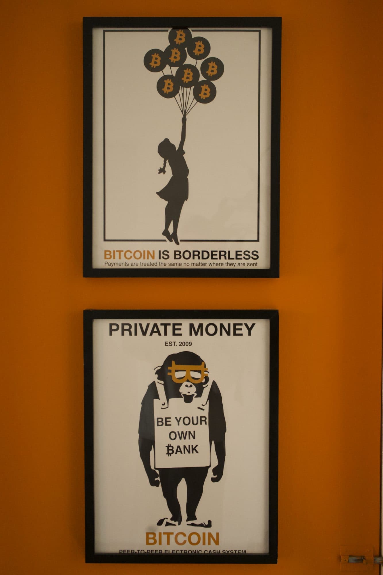 Two Bitcoin posters on an orange wall: Bitcoin is borderless, and Private money