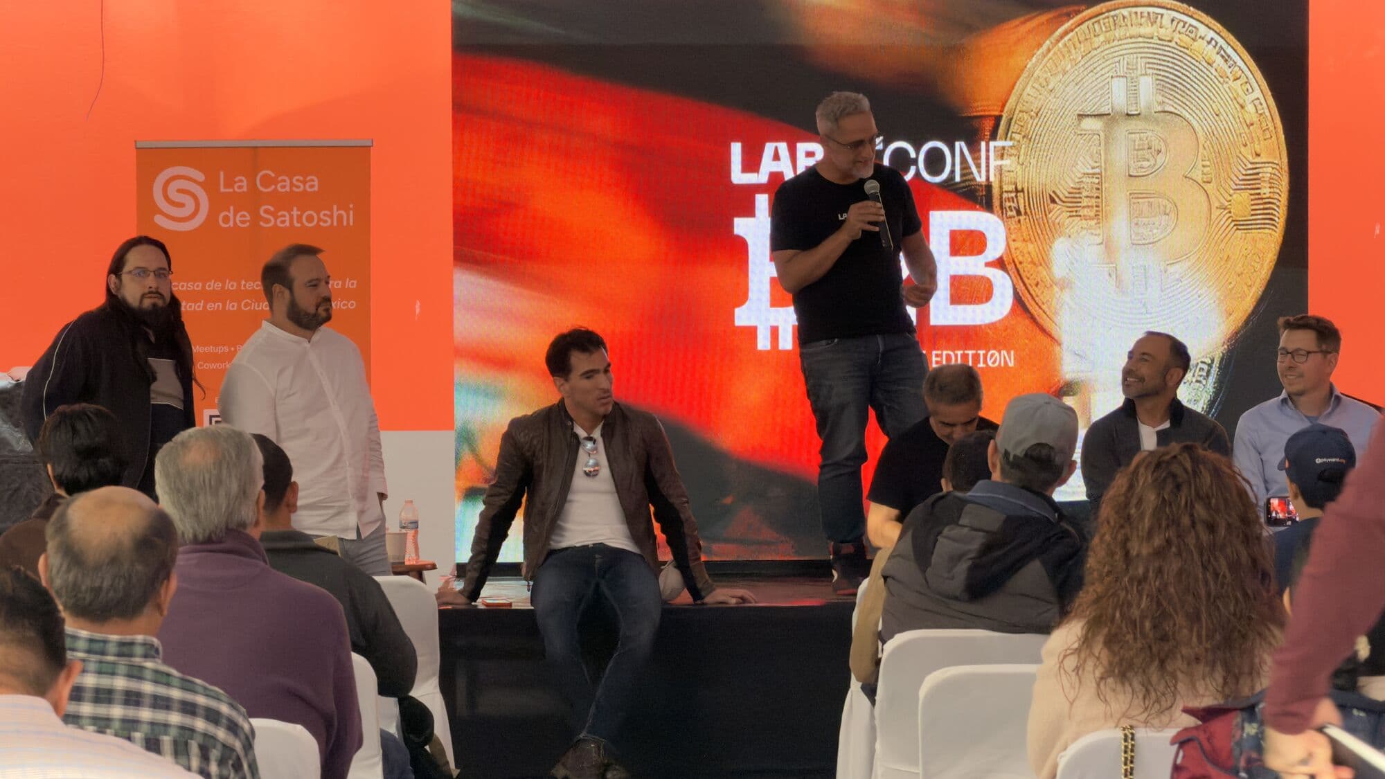 Un panel en el escenario de LABITCONF B2B, con el banner de La Casa de Satoshi a la izquierda
