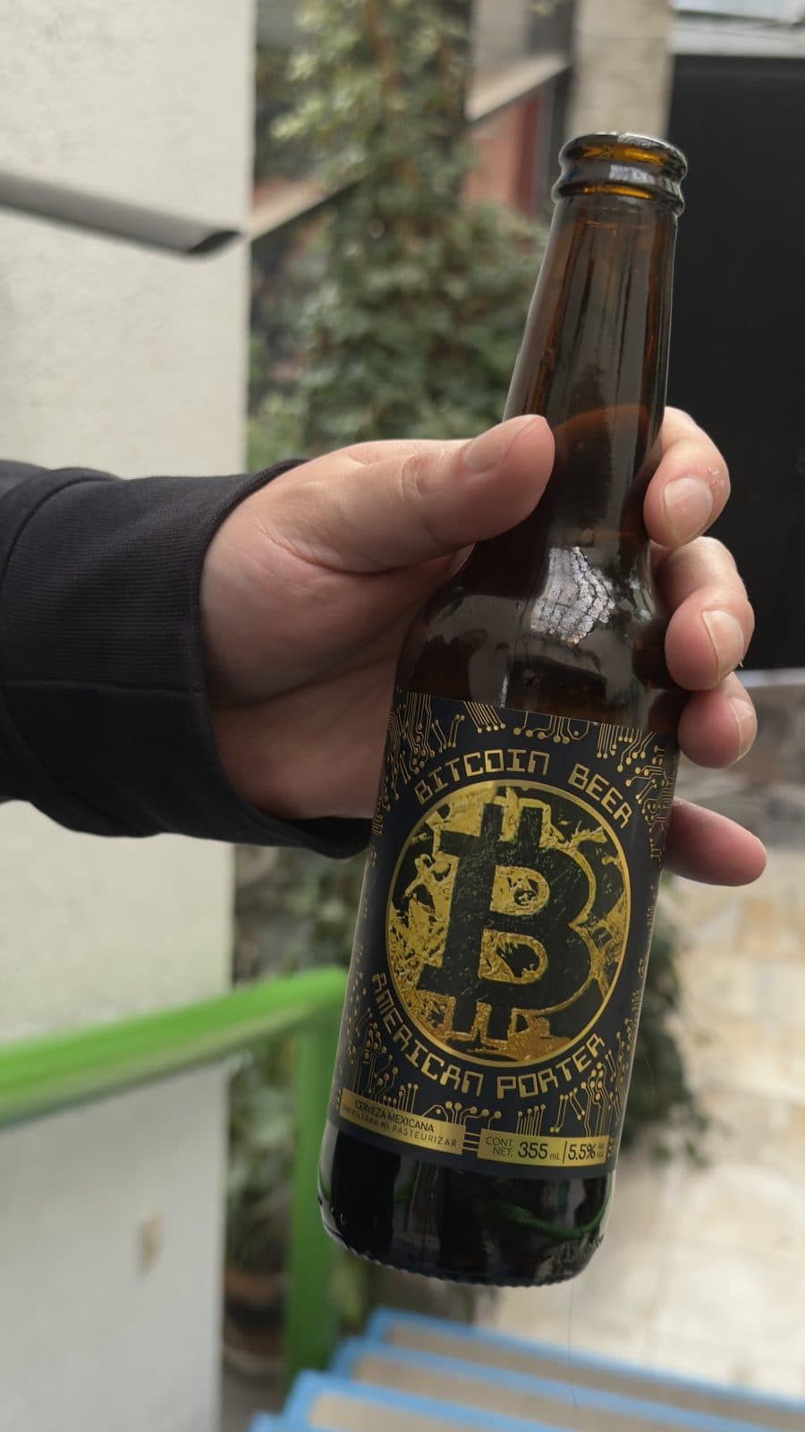 A bottle of Bitcoin Beer American porter held up in the garden
